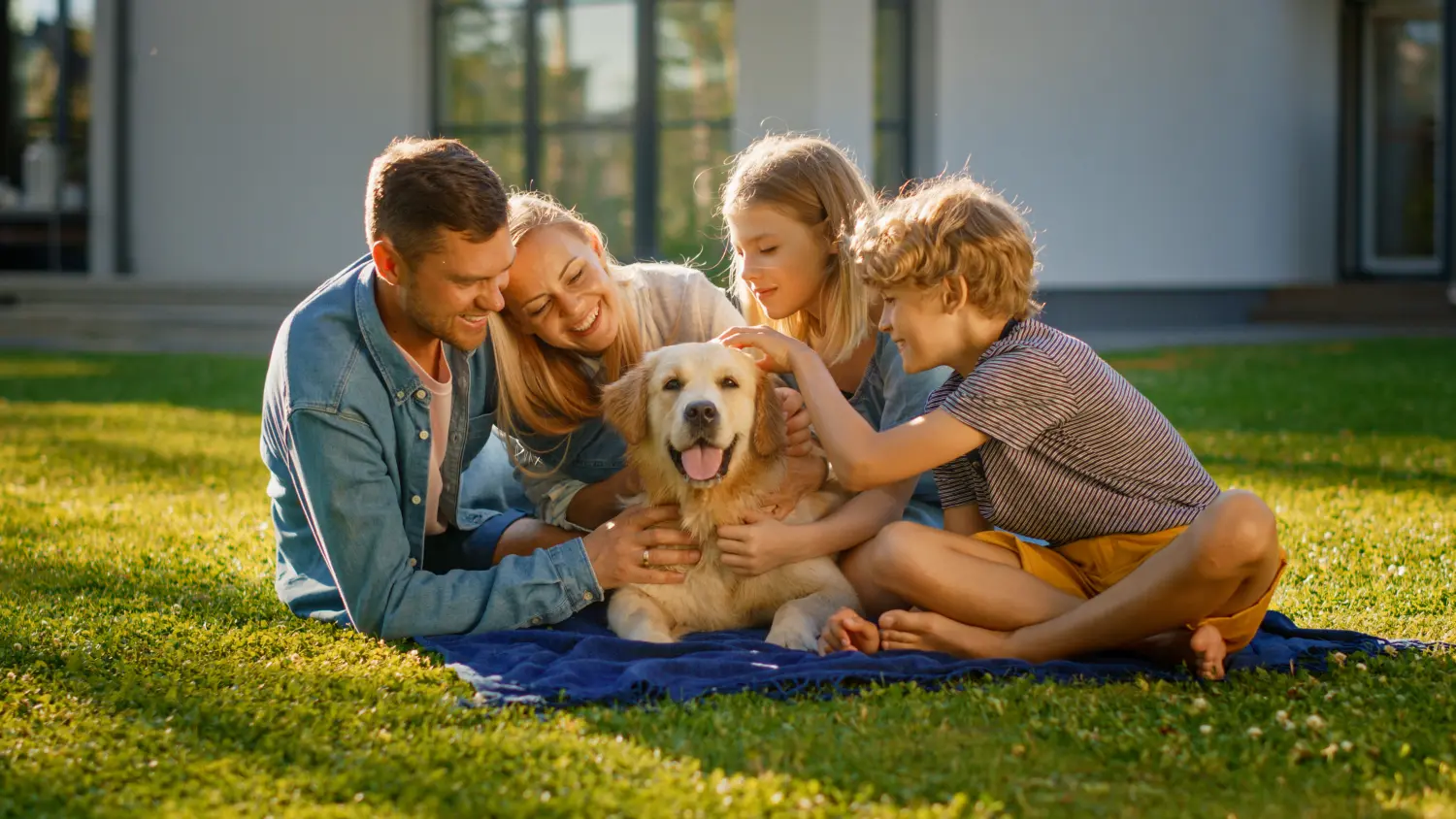 Lächelndes Porträt einer schönen vierköpfigen Familie, die auf dem Rasen picknickt und mit einem glücklichen Golden Retriever Hund posiert.